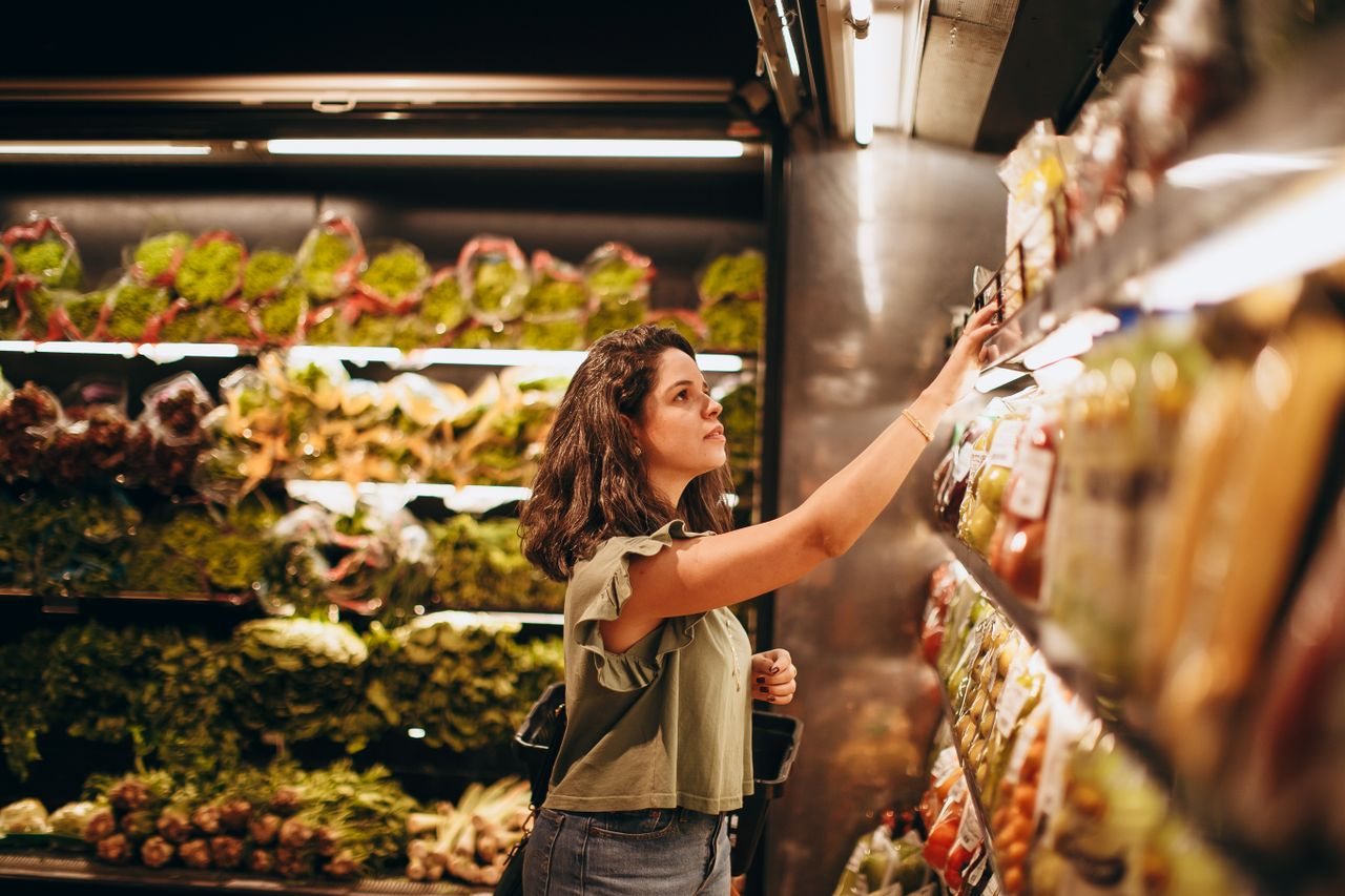 Free A woman selects fresh vegetables in a well-lit supermarket produce aisle. Stock Photo
